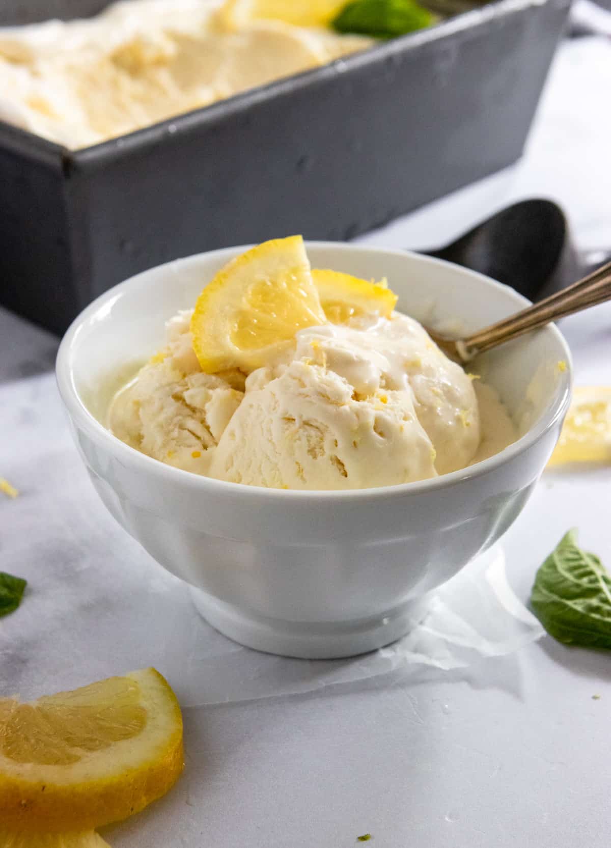 Scoop of homemade lemon ice cream in white bowl with spoon.