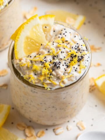 Lemon poppy seed overnight oatmeal in glass jar with lemon slices and poppy seeds on top for garnish.