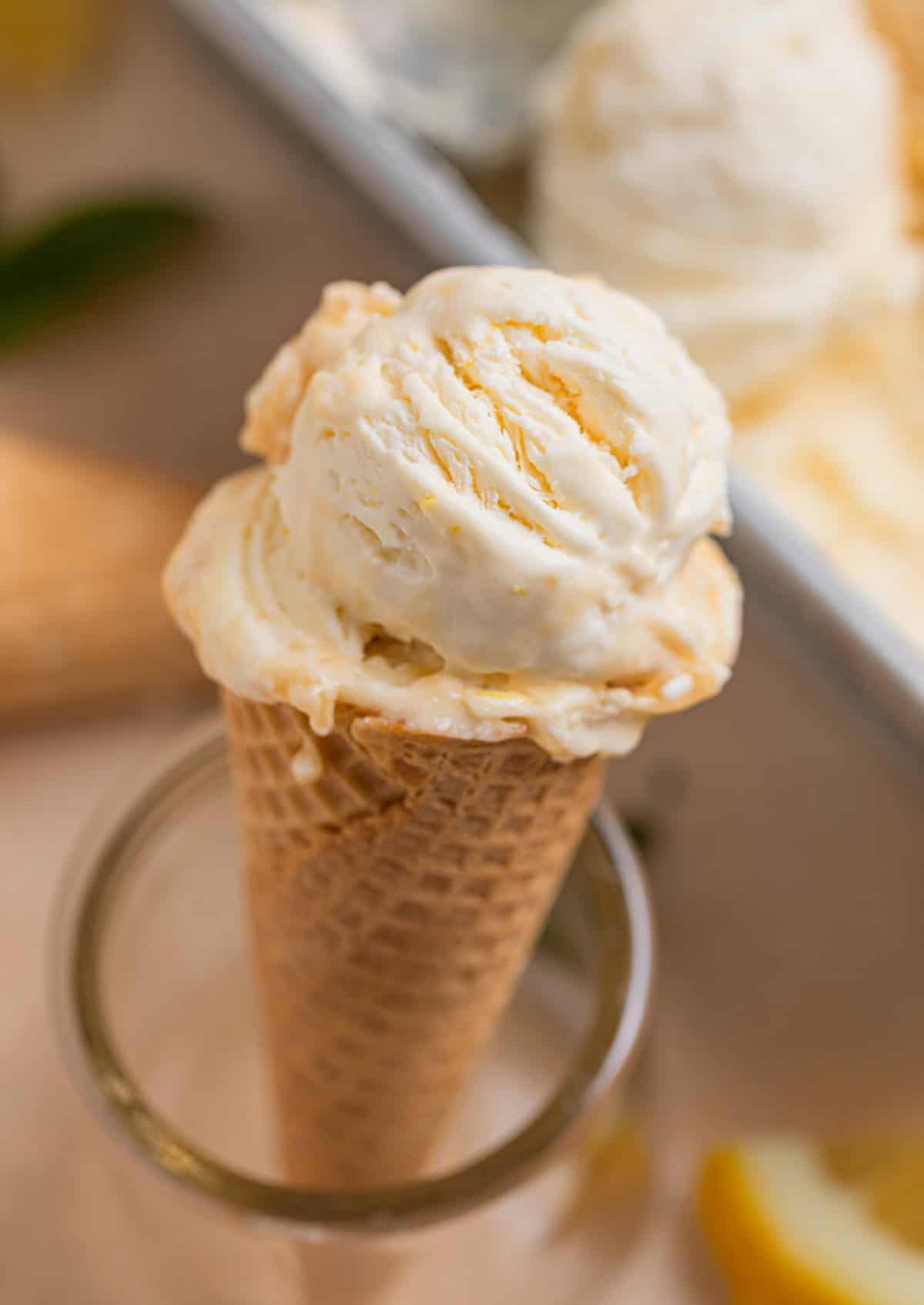 Sugar ice cream cone topped with no churn lemon ice cream propped up in glass.