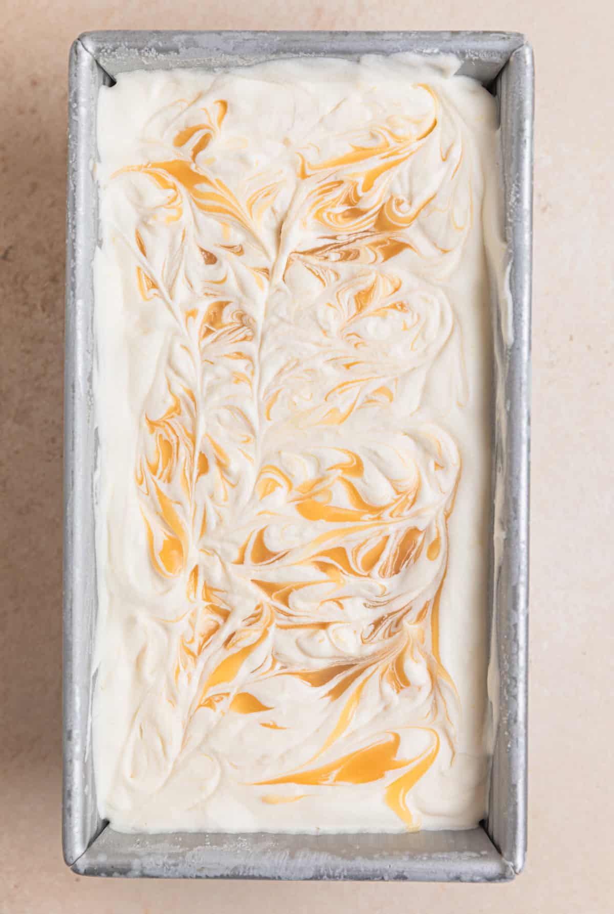 Frozen homemade lemon ice cream in container with lemon curd swirls.