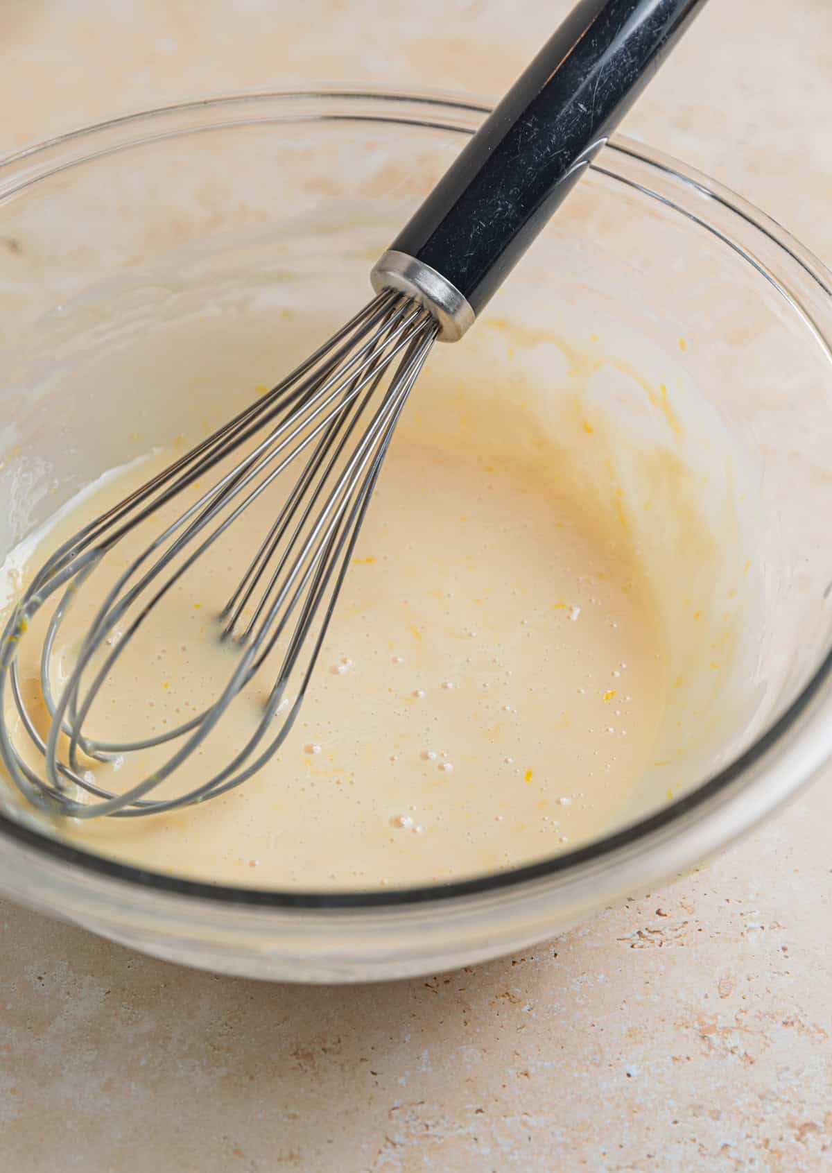 Sweetened condensed milk, lemon zest, lemon juice and vanilla whisked together in glass bowl with whisk propped in the bowl.