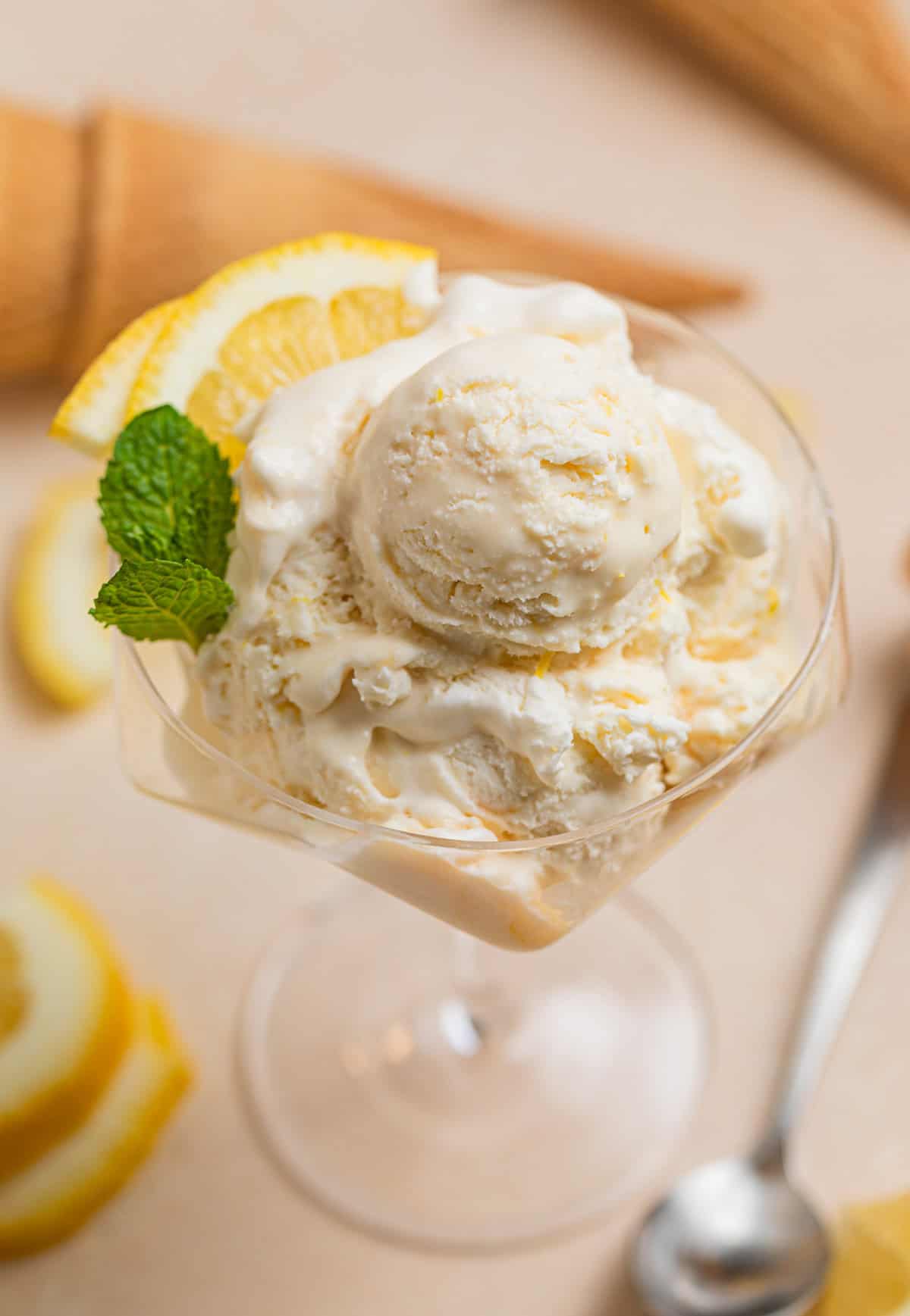 Serving glass with no churn lemon ice cream scooped with lemon slices and fresh mint.