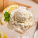 Scooped lemon ice cream in stemware with two lemon quarters and fresh mint leaves.