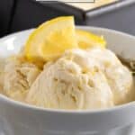 No churn lemon ice cream scooped in white dish with lemon slices for garnish.