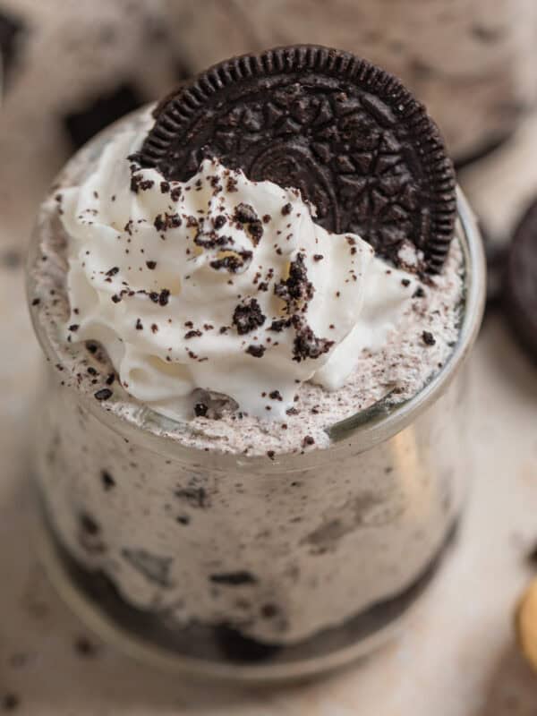 Oreo cheesecake cups topped with whipped cream and an Oreo along with more cookie crumbs.