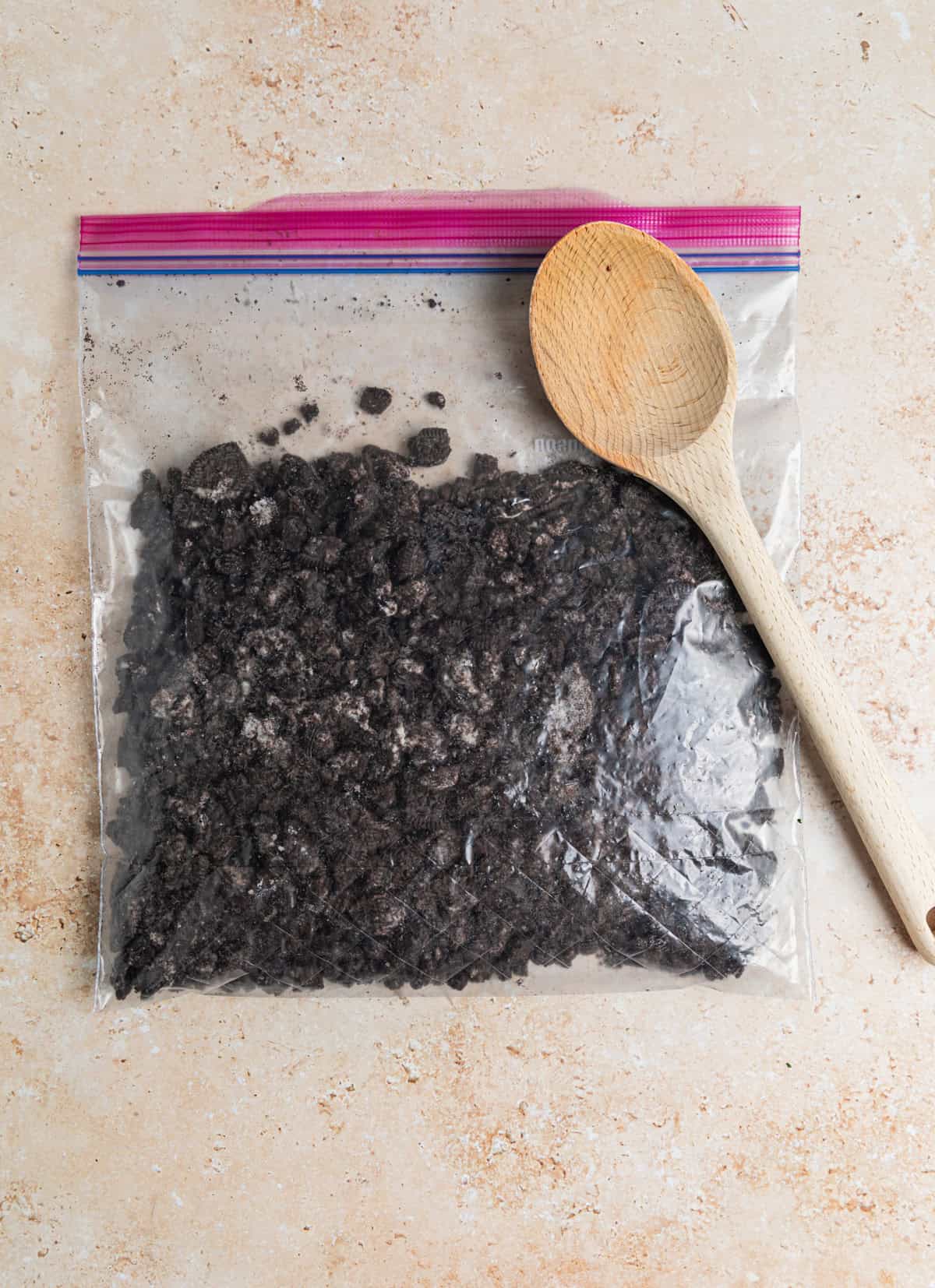Crushed Oreos in plastic bag with wooden spoon set on top.