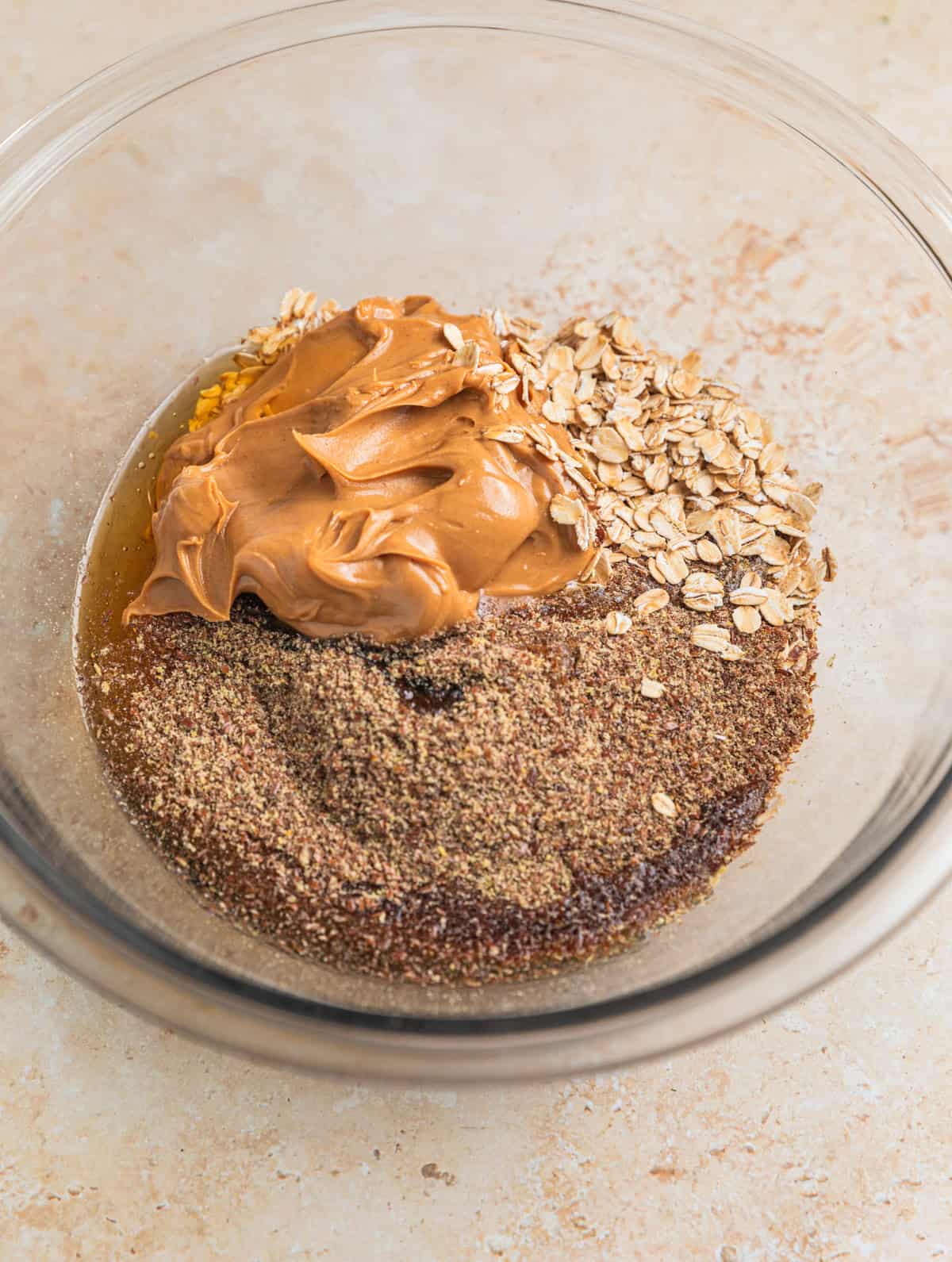 Peanut butter, oats, flax, maple and honey in glass mixing bowl.