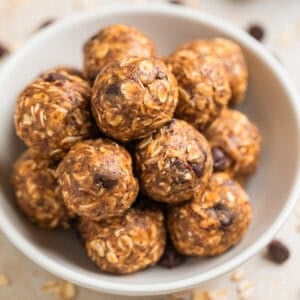 White ceramic bowl with peanut butter oatmeal energy bites with chocolate chips and oats scattered around the bowl.