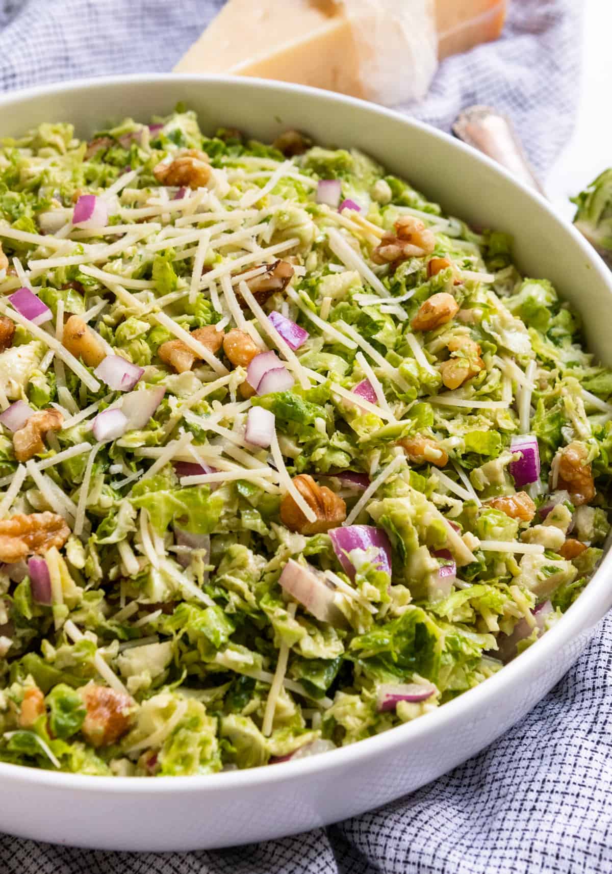 Shaved Brussel Sprout Salad in white bowl with shredded parmesan.