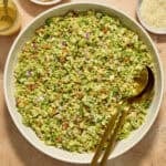 Brussels sprout salad in bowl with serving utensils, topped with shredded parmesan cheese.