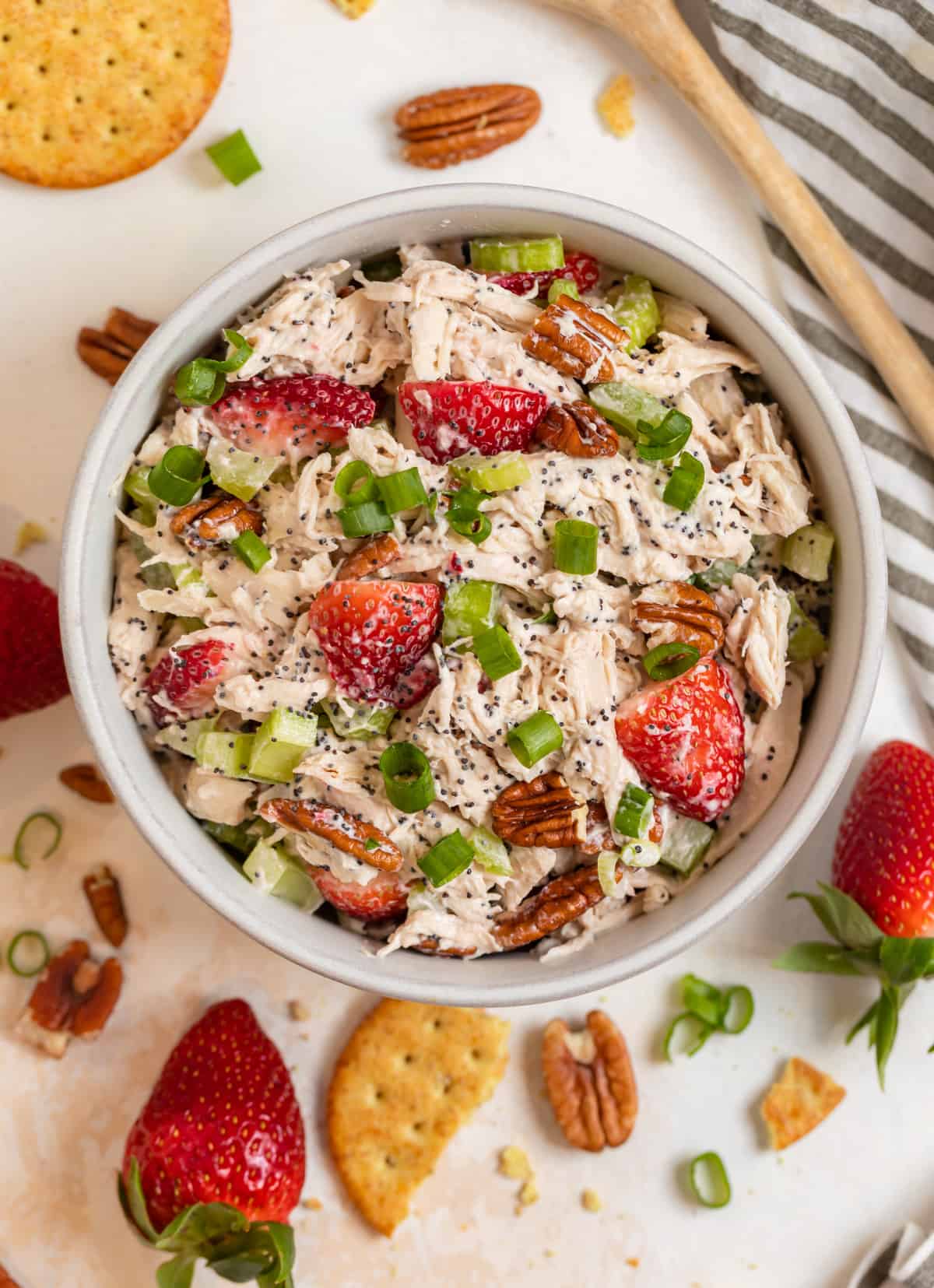 Strawberry poppy seed pecan chicken salad in bowl with crackers and strawberries surrounding.