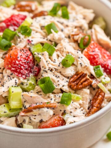 White bowl with strawberry pecan chicken salad topped with green onion and pecans.