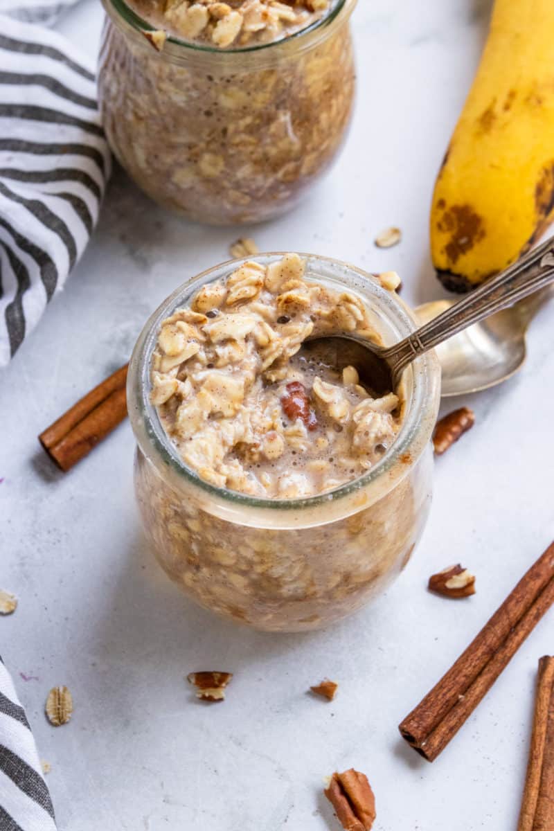 Spoon in jar with oatmeal and banana and cinnamon sticks.