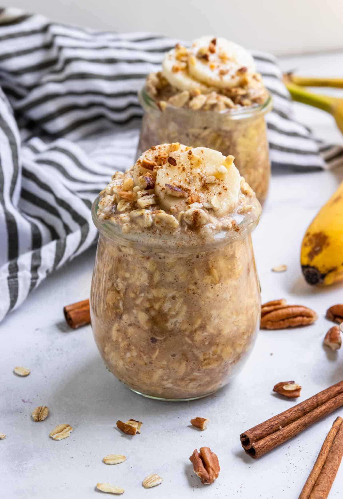 Oatmeal in glass jars with banana slices and pecans.