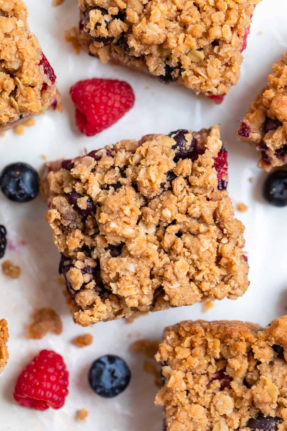 Berry crumble bars with oat topping on parchment with fresh berries surrounding.