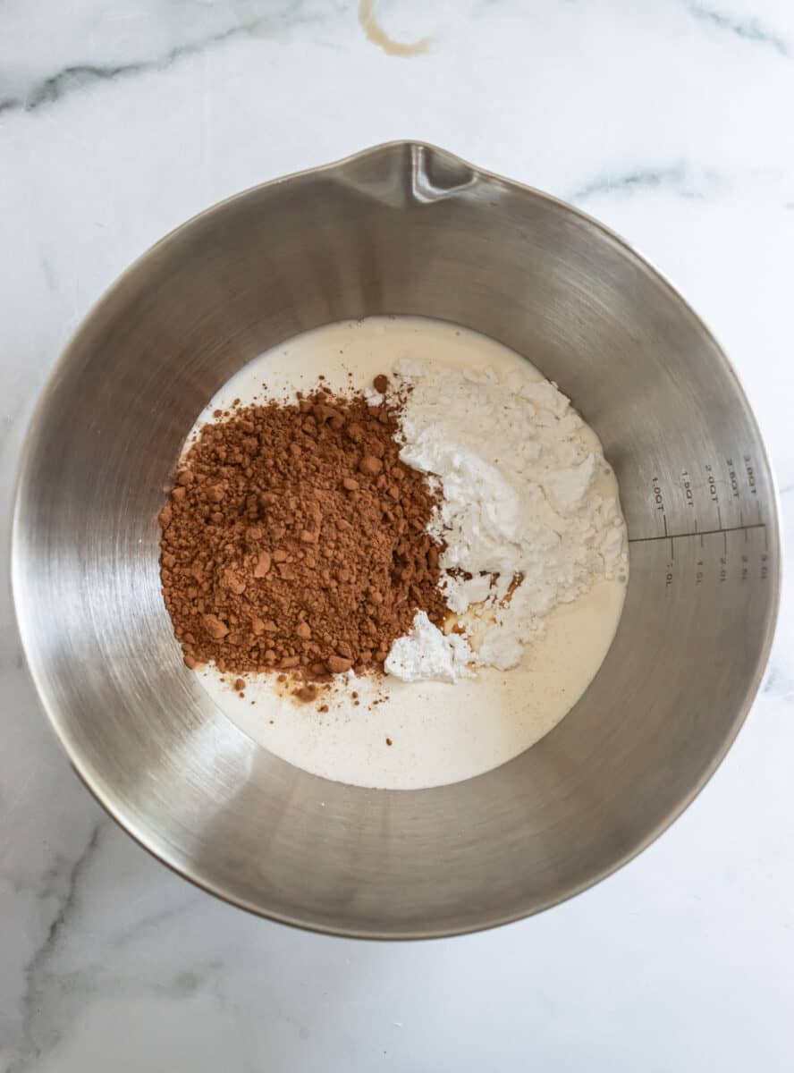 Heavy cream, cocoa powder, and confectioner's sugar in stainless steel mixing bowl.