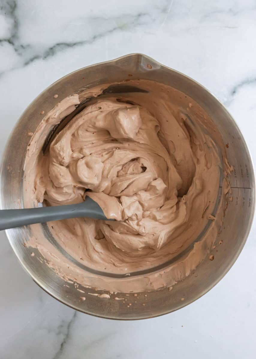 Chocolate whipped cream with stiff peaks in bowl with gray spatula.