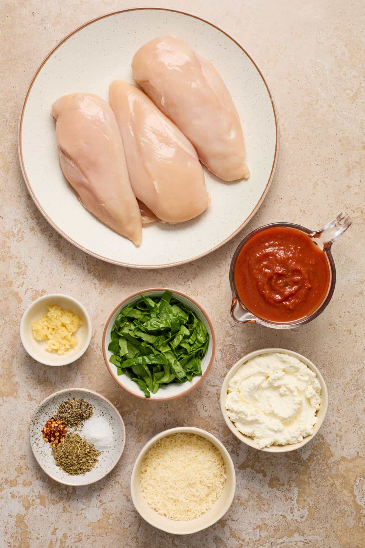 Chicken breast, marinara, spinach, parmesan and other ingredients on surface.