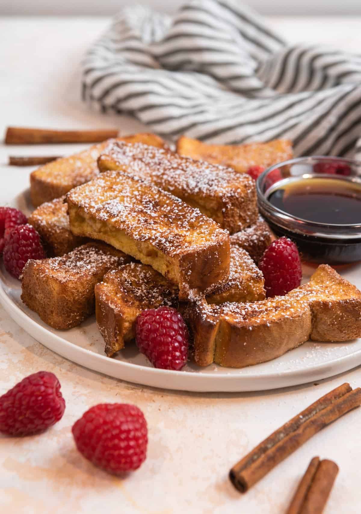 White dish with air fryer French Toast sticks with powdered sugar and raspberries.