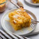Honey cornbread on plate with butter and honey drizzle.