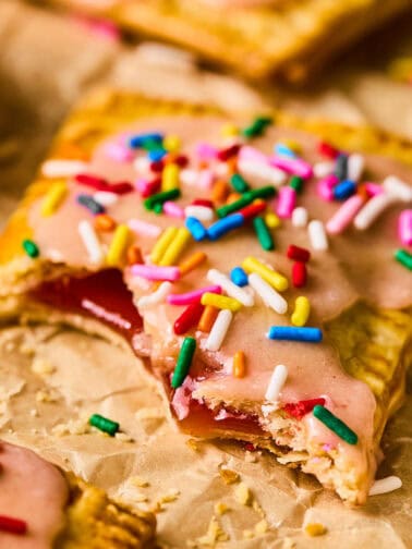 Homemade pop tart with pie crust on parchment with bite taken out.