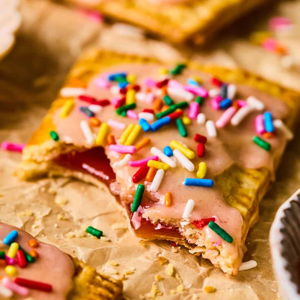Homemade pop tart with pie crust on parchment with bite taken out.