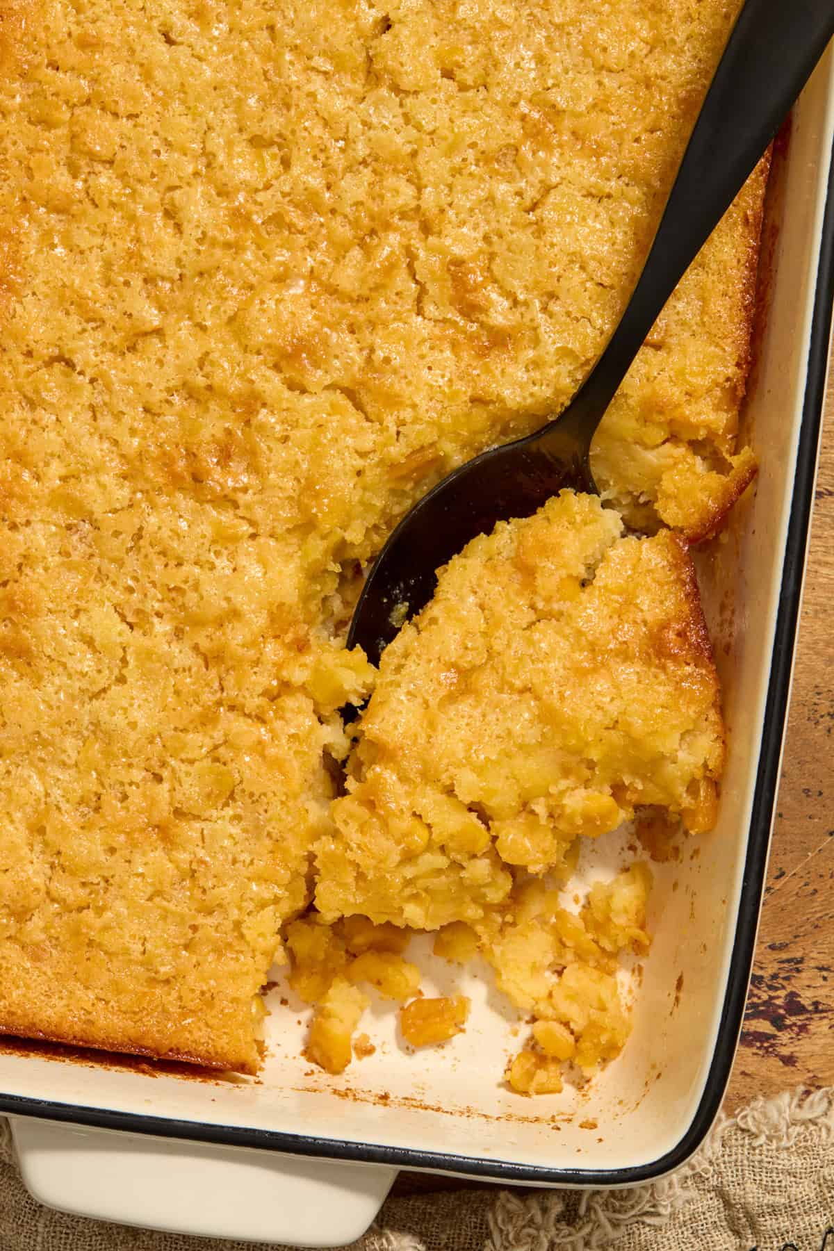 Cornbread casserole in dish with serving spoon scooping in. 