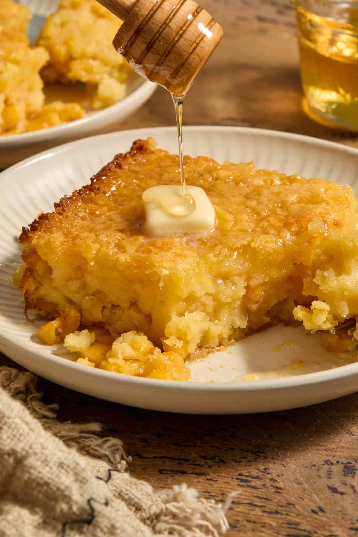 Honey cornbread casserole served on plate with honey drizzling over butter on top.