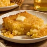 Sweet jiffy cornbread casserole on plate with honey drizzling over top.