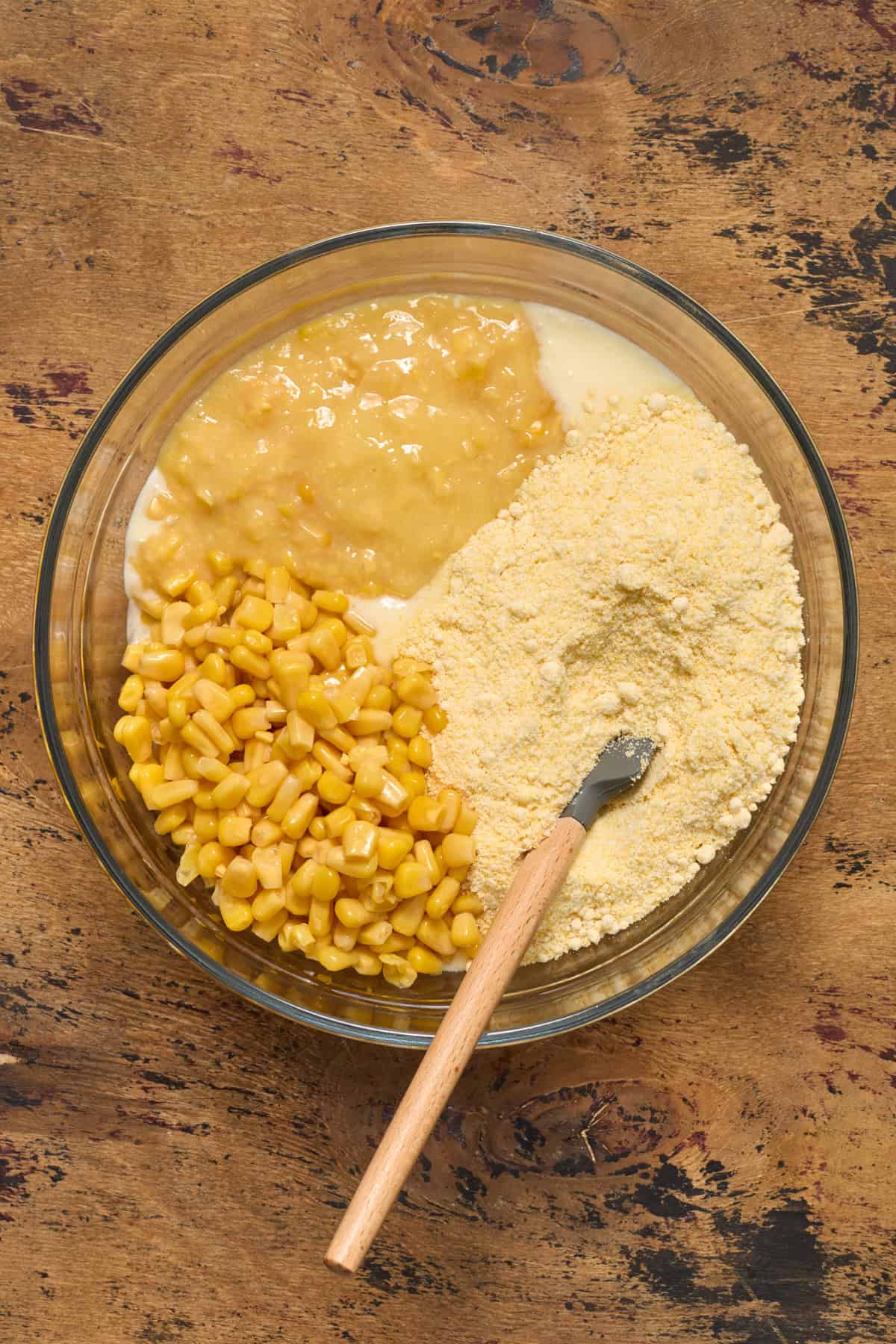 Cornbread mix, corn and creamed corn in bowl with spatula.