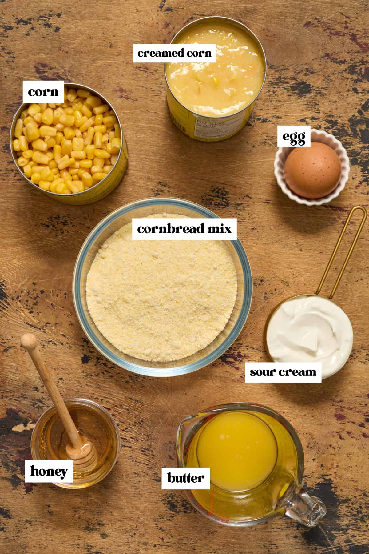 Cornbread mix, honey, creamed corn and other ingredients arranged on surface.