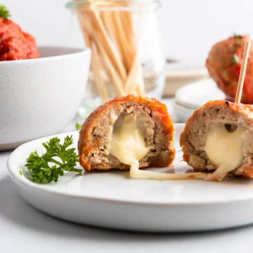 Mozzarella stuffed turkey meatballs on plate with cheese stretching.