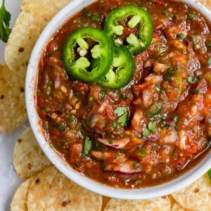 Overhead shot of bowl of salsa with chips and jalapeños.