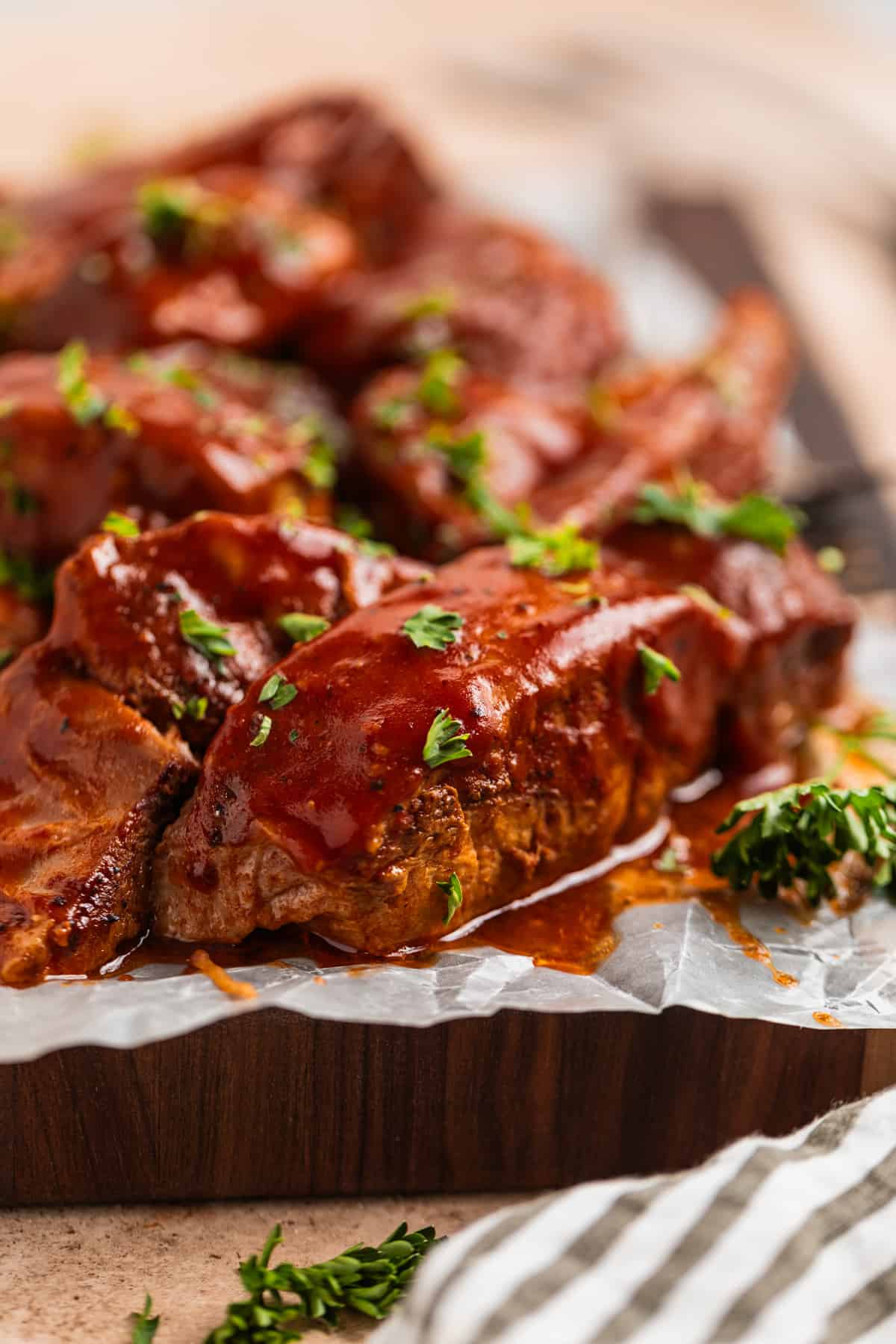 Country style BBQ ribs on wood board topped with wax paper and topped with parsley.