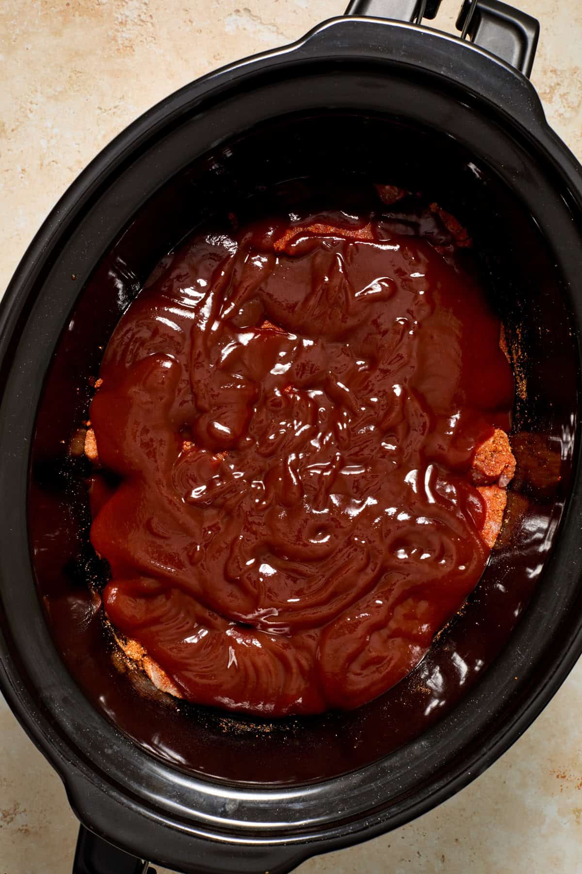 BBQ sauce poured over meat in crockpot.