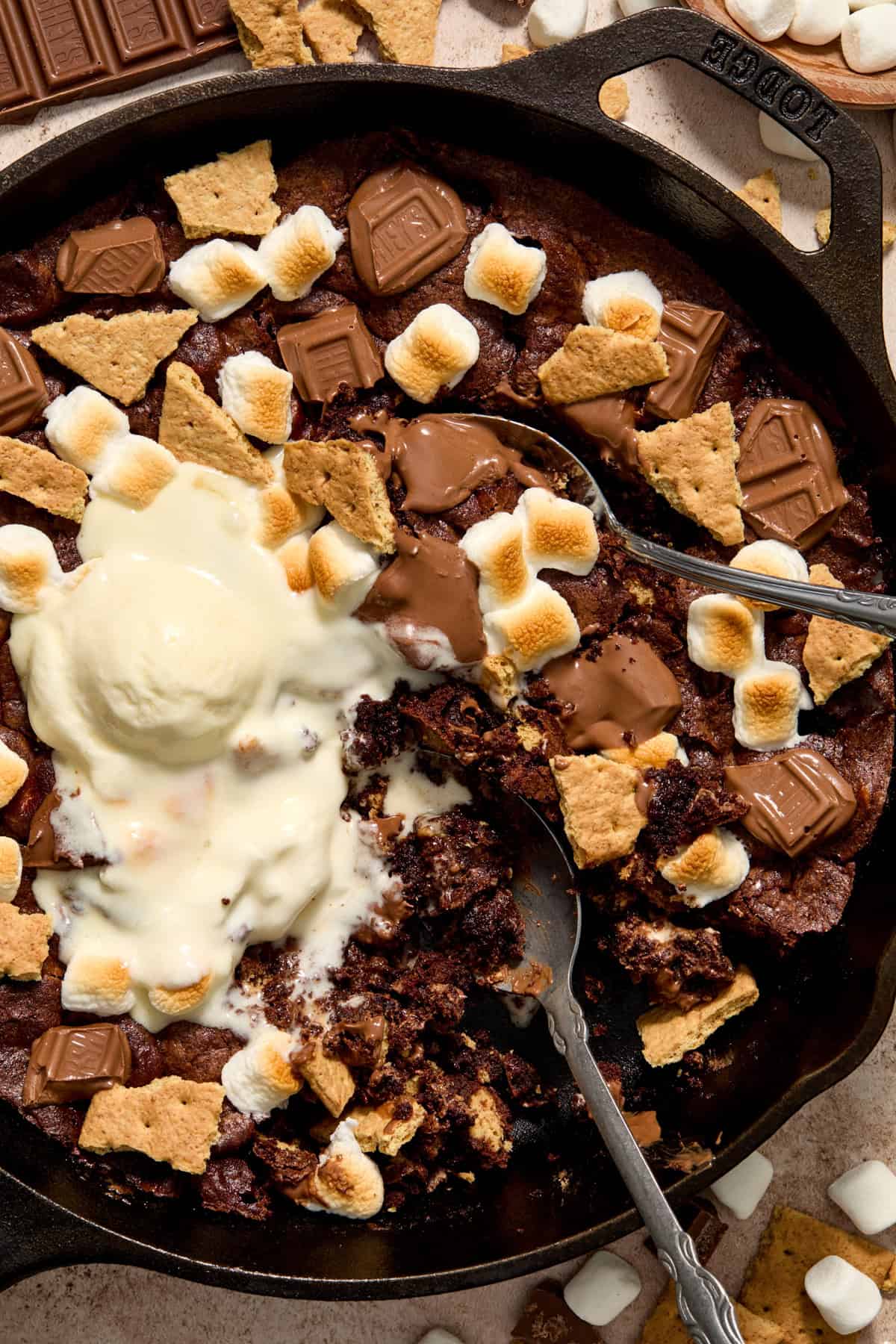 Overhead view of s'mores brownie in cast iron skillet with two spoons scooping into the brownie.