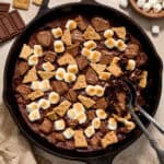 Brownie in skillet topped with marshmallows, chocolate bars and pieces of graham crackers.