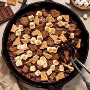 Brownie in skillet topped with marshmallows, chocolate bars and pieces of graham crackers.