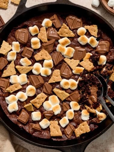 Brownie in skillet topped with marshmallows, chocolate bars and pieces of graham crackers.