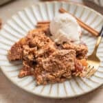 Apple dump cake recipe scooped on dessert dish with scoop of vanilla ice cream and cinnamon sticks.