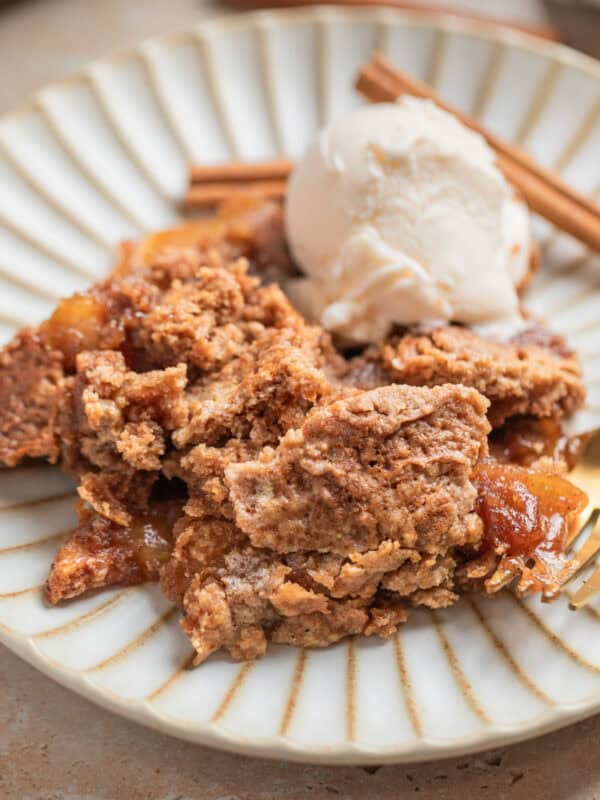 Apple dump cake recipe scooped on dessert dish with scoop of vanilla ice cream and cinnamon sticks.