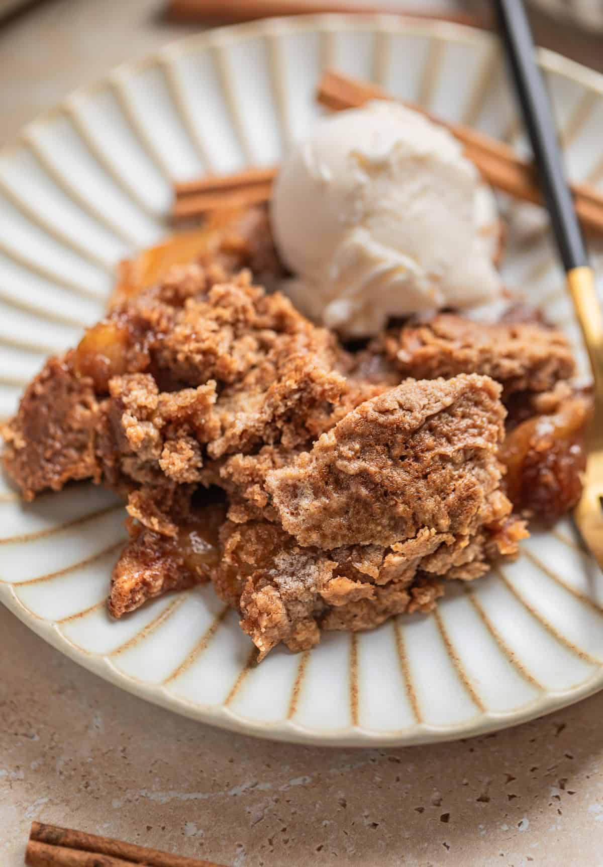 Apple dump cake served on dish with fork and scoop of vanilla ice cream.