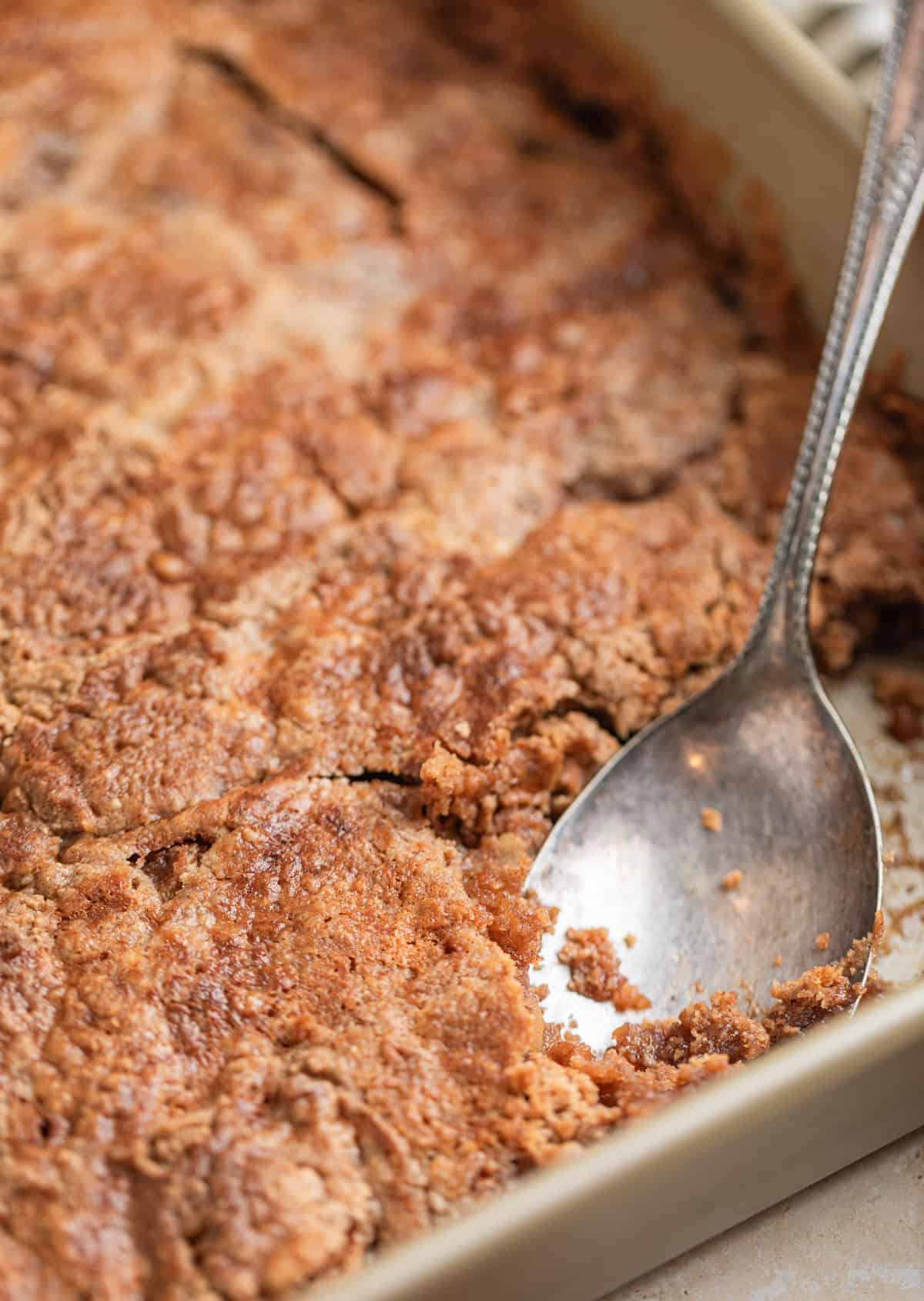 Serving spoon scooping into pan with apple dump cake.