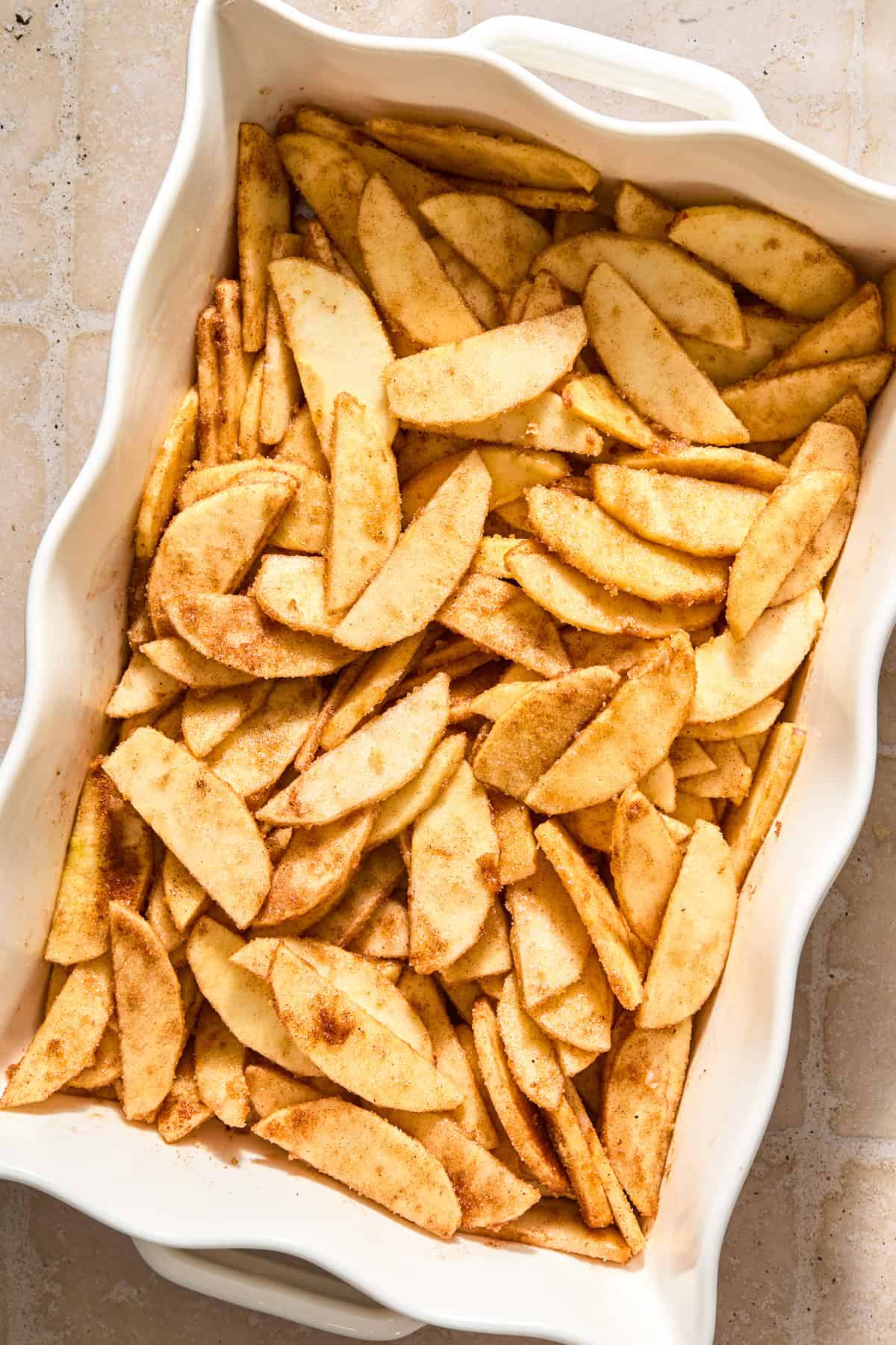 Sliced apples tossed with cinnamon and sugars in baking dish.