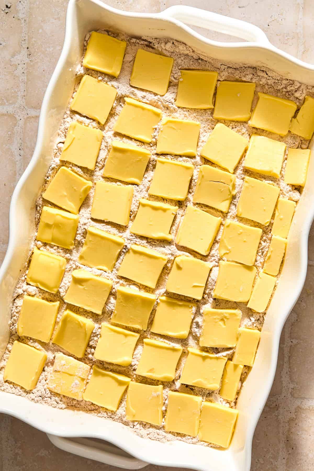 Pieces of butter arranged in a grid over top of cake mix in pan.