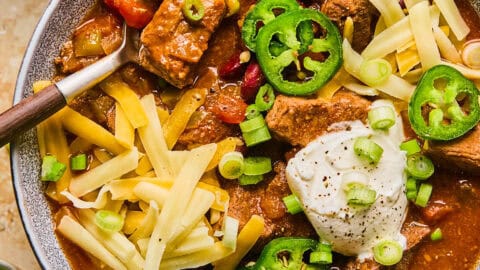 Bowl of chili with brisket, shredded cheese, sour cream and spoon scooping up a spoonful.