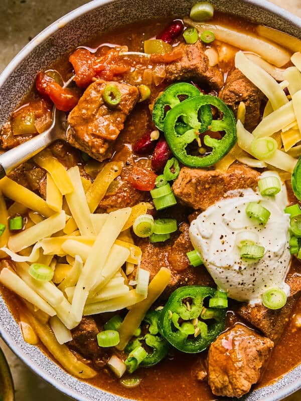 Bowl of chili with brisket, shredded cheese, sour cream and spoon scooping up a spoonful.