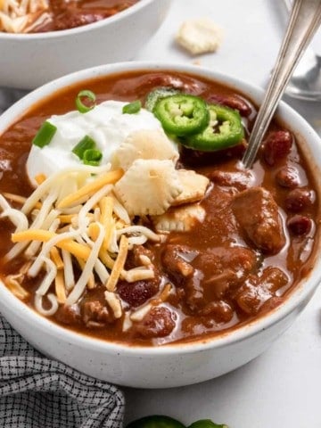 Brisket chili in white bowl with spoon.