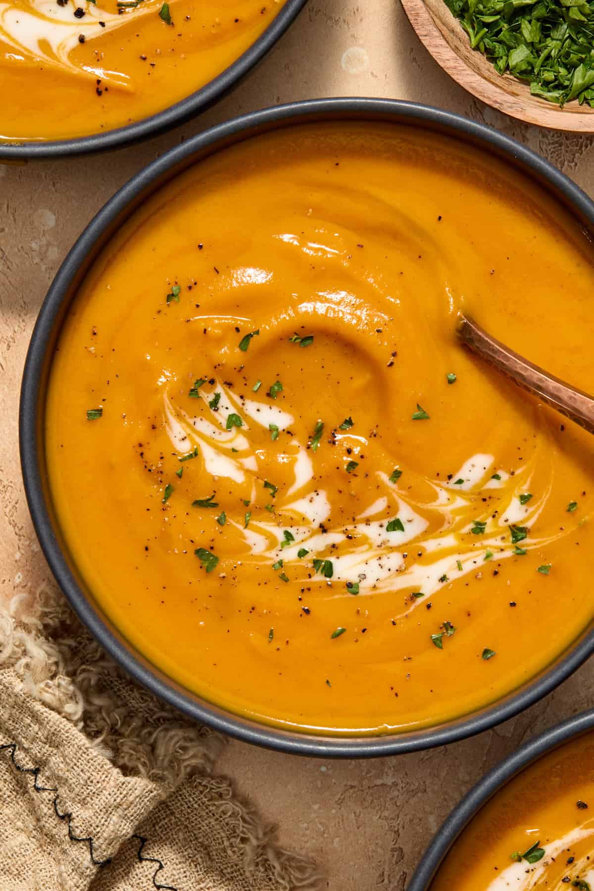 Bowl of carrot and sweet potato soup with cream and herbs swirled over top.