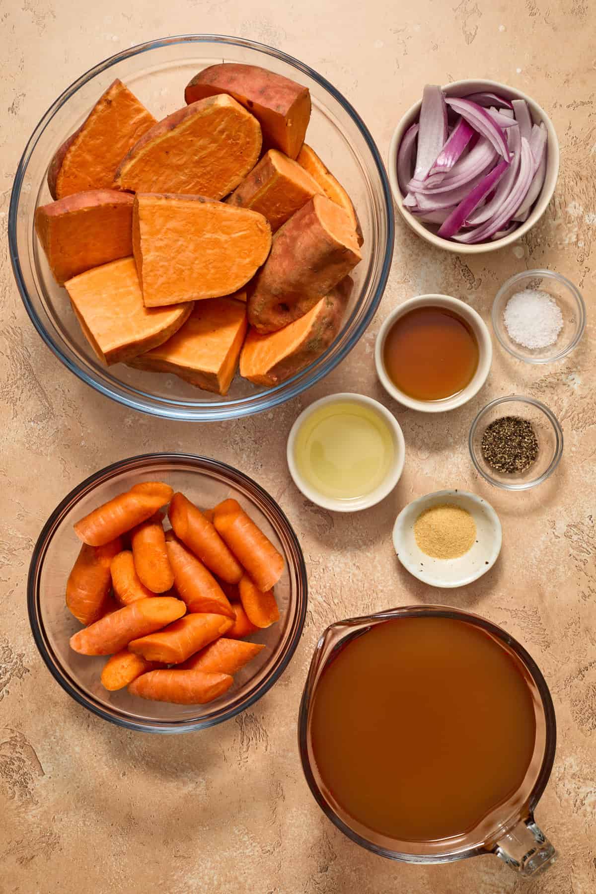 Cut sweet potatoes, onions, carrots, broth and other ingredients needed to make recipe on surface.